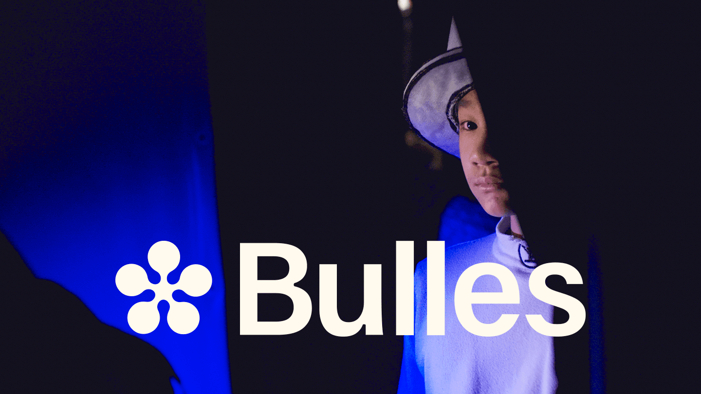Logo de Bulles avec une artiste en costume blanc et chapeau pointu sous un éclairage de scène bleu